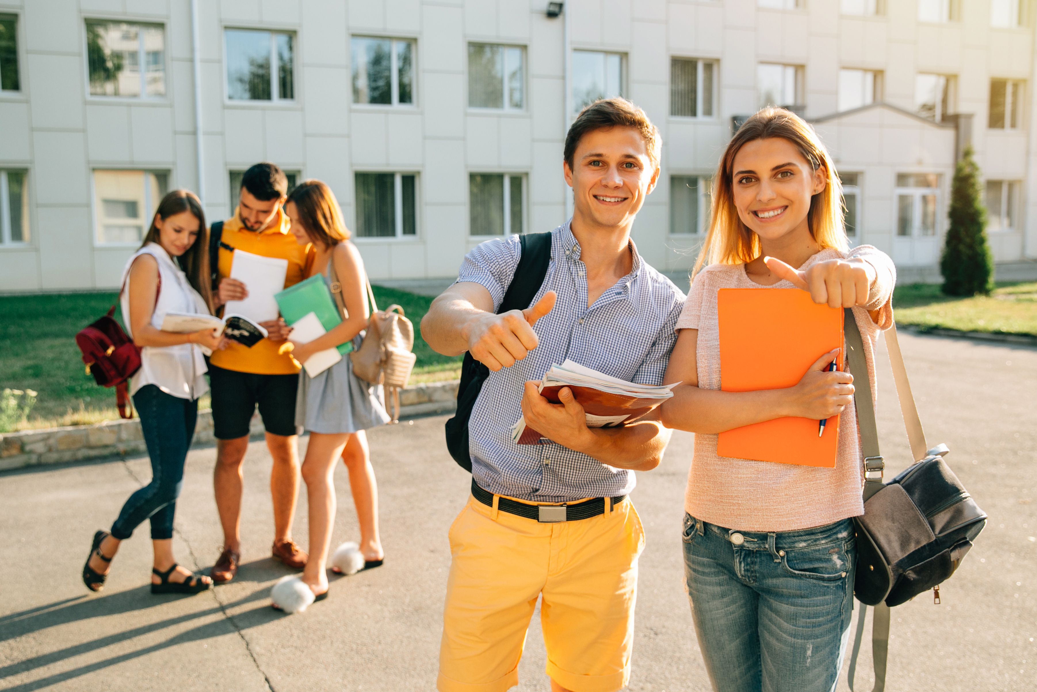 Happy two young students with note-books and backpacks smiling and showing thumb up Happy two young students with note-books and backpacks smiling and showing thumb up